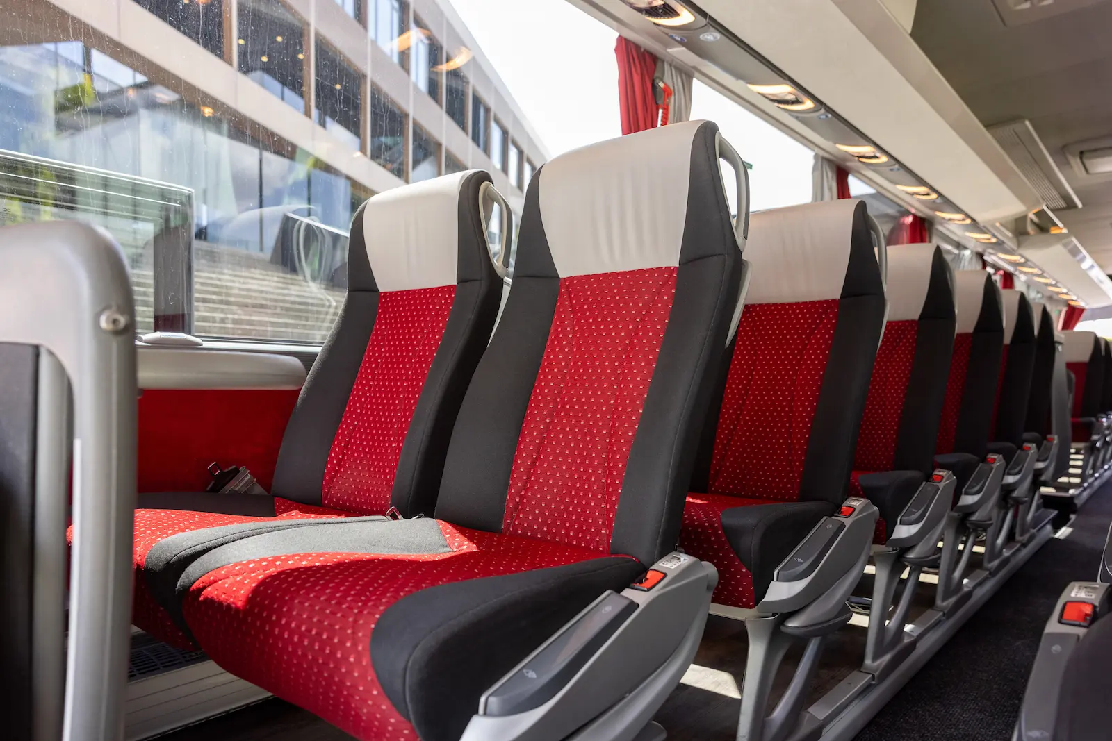 Setra Bus Rücksitzansicht mit bequemen roten Sitzen und modernem Design, geparkt vor einem Gebäude mit großen Fenstern.