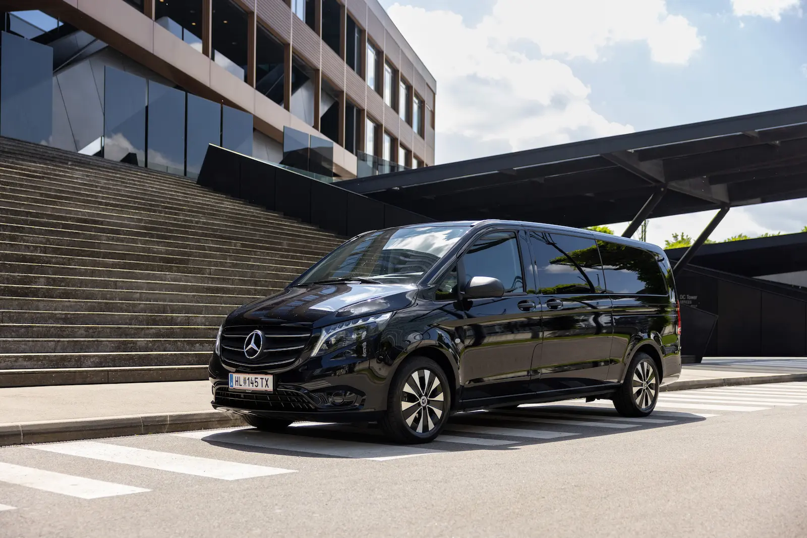 Ein schwarzer Mercedes Benz Vito steht vor einem modernen Gebäude mit Treppen und Glasfassade, ideal für geschäftliche Nutzung.