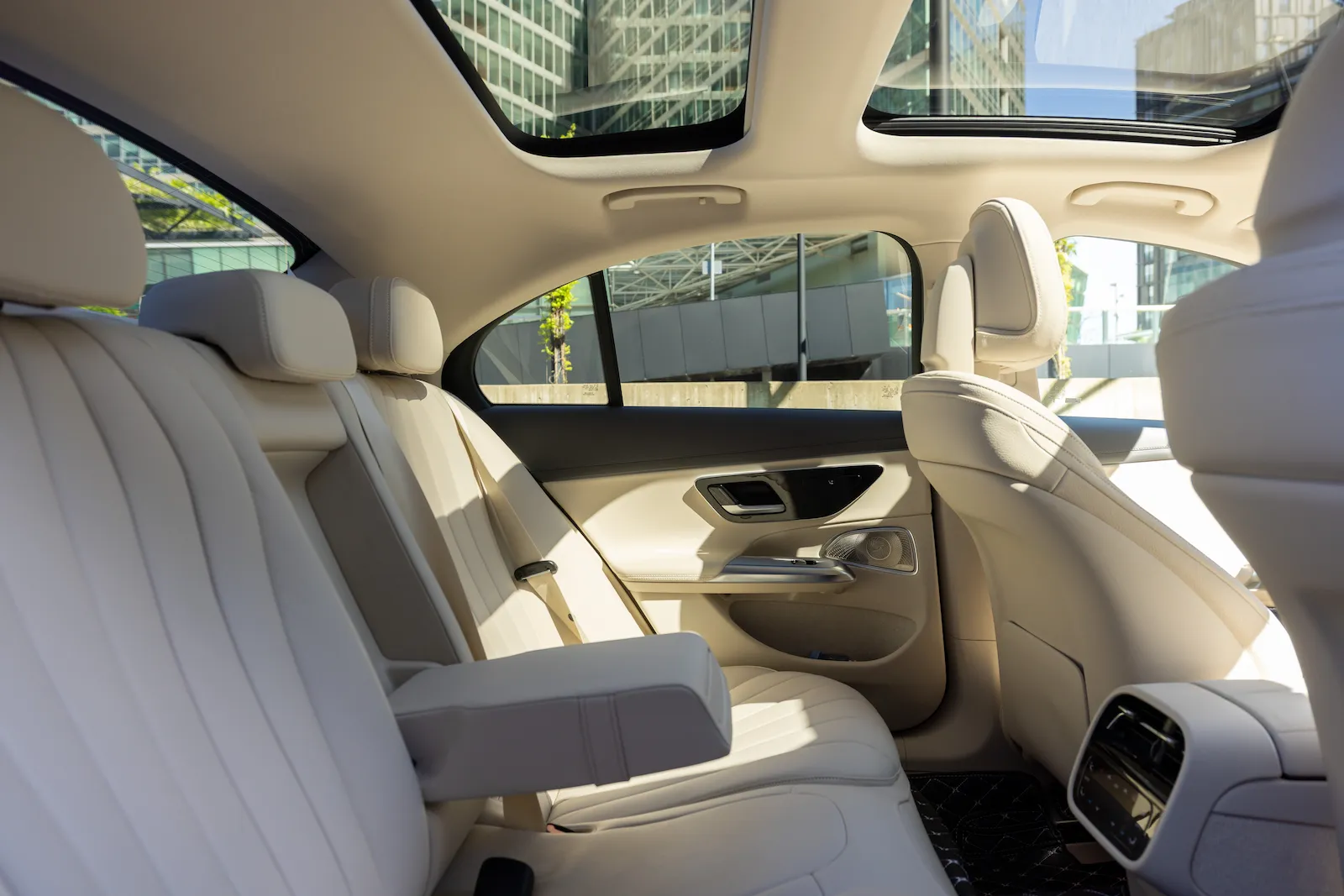 Luxuriöse Mercedes S-Klasse Innenansicht mit bequemen Ledersitzen und Panoramadach vor urbanem Gebäude.