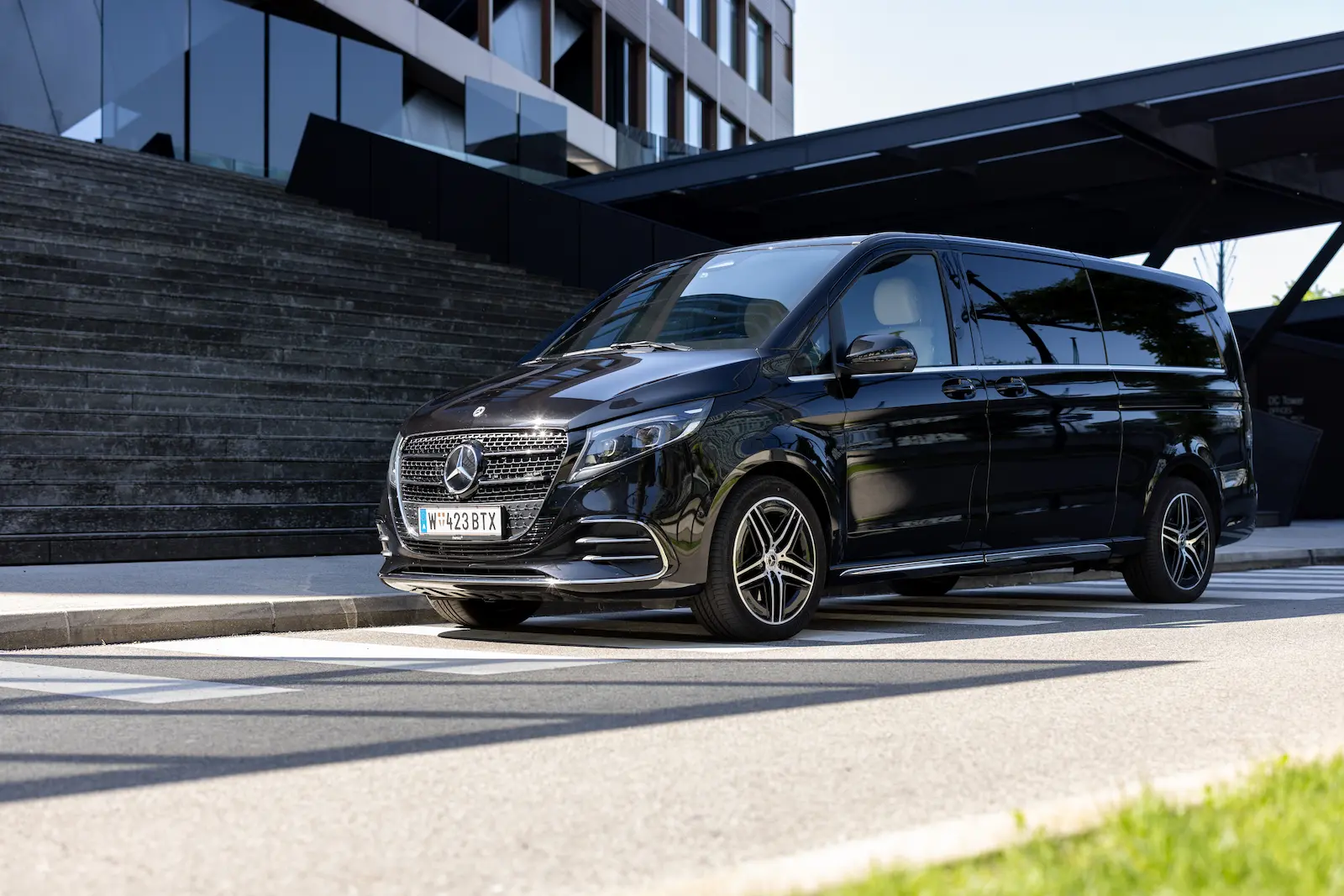 Mercedes Vito front side view featuring a sleek black design, parked near a modern building with a pedestrian crossing in the foreground.