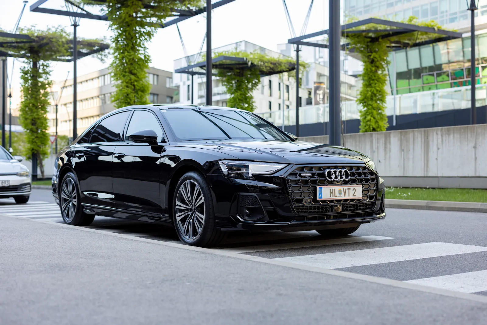 Schwarze Audi A8 geparkt vor einem modernen Gebäude mit grünen Pflanzen und urbanem Hintergrund.