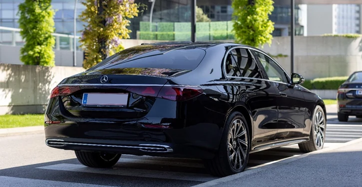 Ein eleganter schwarzer MB E Class Rear Slider steht an einem Zebrastreifen, umgeben von urbaner Umgebung mit Grünpflanzen.