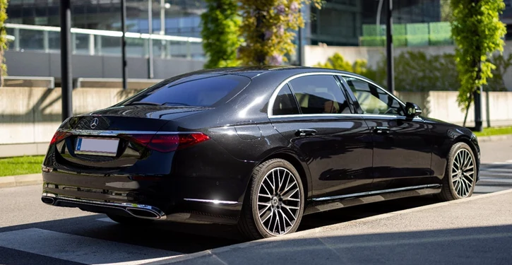 Elegante MB S Class Long Rear View Slider in Schwarz, geparkt vor einem modernen Gebäude mit grünen Pflanzen.