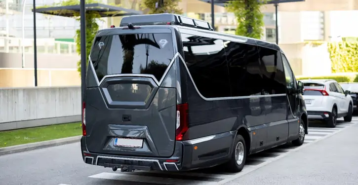 Der MB Sprinter VIP Rear View zeigt die elegante Rückansicht des Luxusvans mit modernem Design, geparkt auf einer Straße mit grünem Hintergrund.