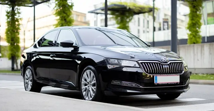 Elegante Skoda Superb Front Slider in Schwarz, geparkt vor einem modernen Gebäude mit grünen Pflanzen.