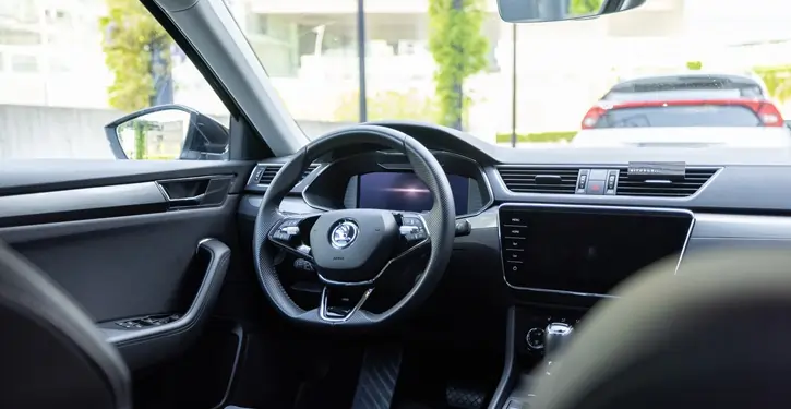 Moderne Skoda Superb Inside View Front Slider mit luxuriösem Lenkrad und Touchscreen, geparkt vor einem urbanen Hintergrund.
